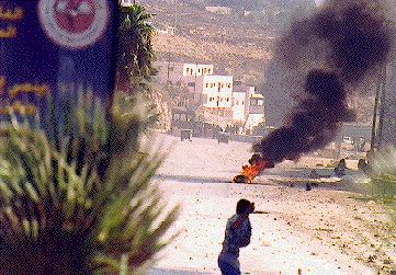 Photo: Smoky haze, burning tire and protestor throwing stone