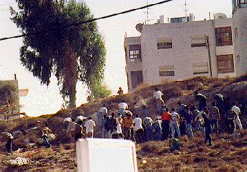 Photo: Scene of a hill opposite covered with people throwing stones